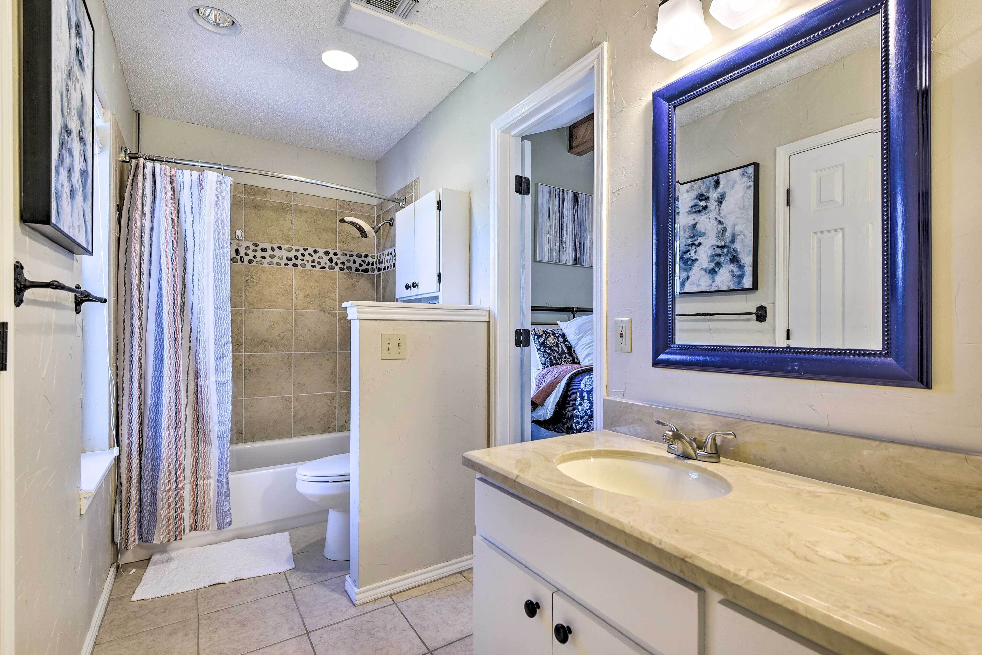 A bathroom with a bathtub, toilet, vanity with a sink, and a mirror.