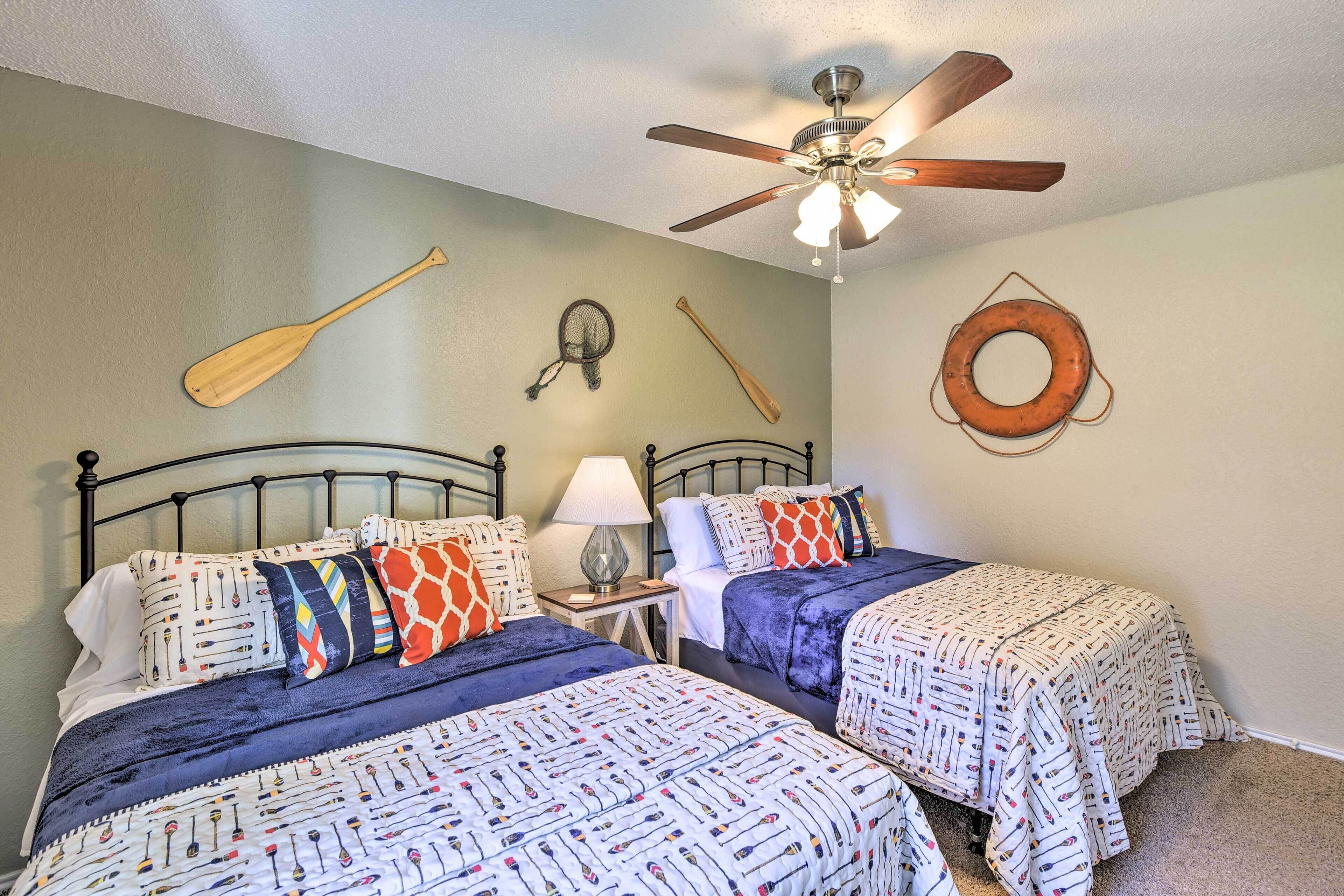 A bedroom with two beds, a ceiling fan, and wall decorations including a paddle, a fishing net, a baseball bat, and a tire.