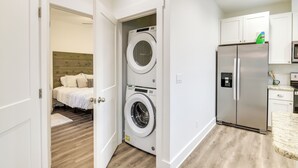 Une petite buanderie équipée d’un lave-linge et d’un sèche-linge, ainsi que d’un réfrigérateur, et une chambre adjacente avec un lit.