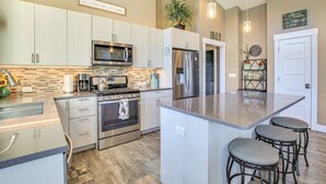 A modern kitchen with stainless steel appliances, a large island with bar stools, and a hanging light fixture. - 'gorge Retreat' - Modern Carson Home w/ Mtn Views! (Carson)