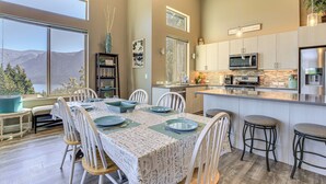 A modern kitchen with a large island, a dining area with a table set for six, and a view of mountains through large windows. - 'gorge Retreat' - Modern Carson Home w/ Mtn Views! (Carson)