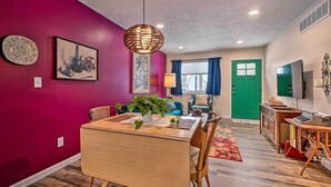 A dining area with a wooden table and chairs, a hanging light fixture, and a colorful rug.