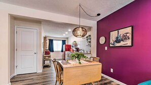 A dining area with a wooden table and chairs, a hanging light fixture, and a purple wall with a framed artwork.