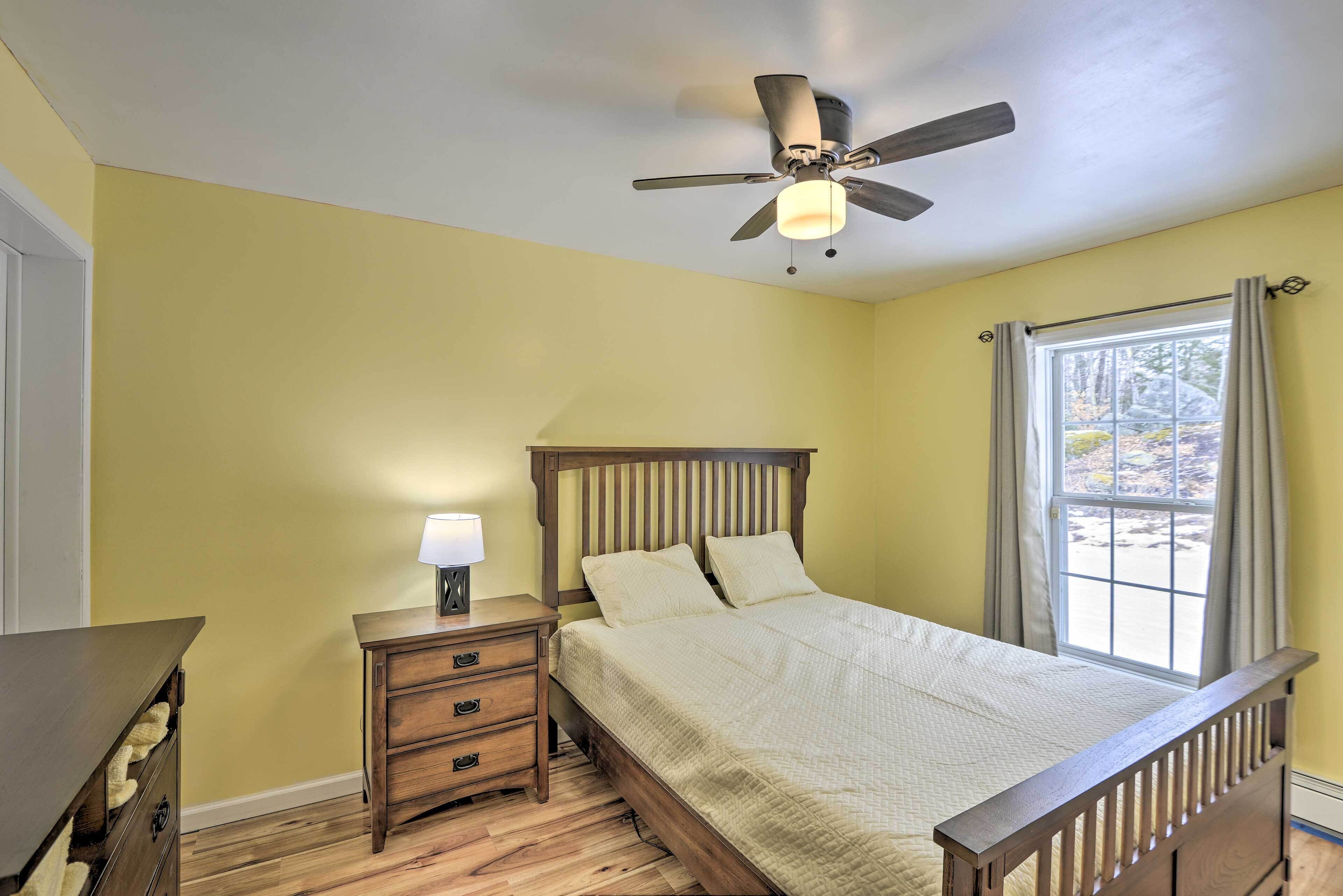 A bedroom with a bed, nightstand, dresser, ceiling fan, and window with curtains.