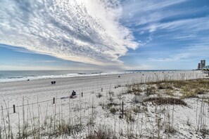 Ein Strand mit einer Person, die auf einem Stuhl sitzt, einem Zaun und etwas Vegetation.
