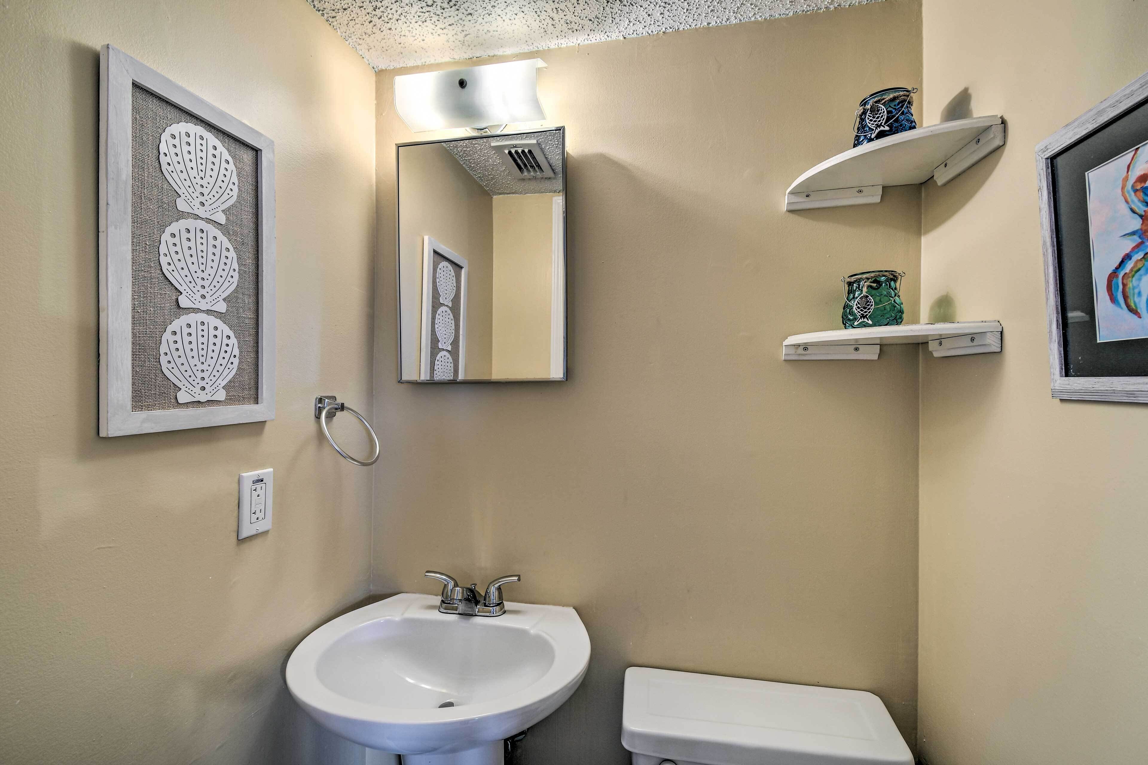 Un bagno con lavandino bianco, un water, uno specchio e mensole decorative con oggetti.