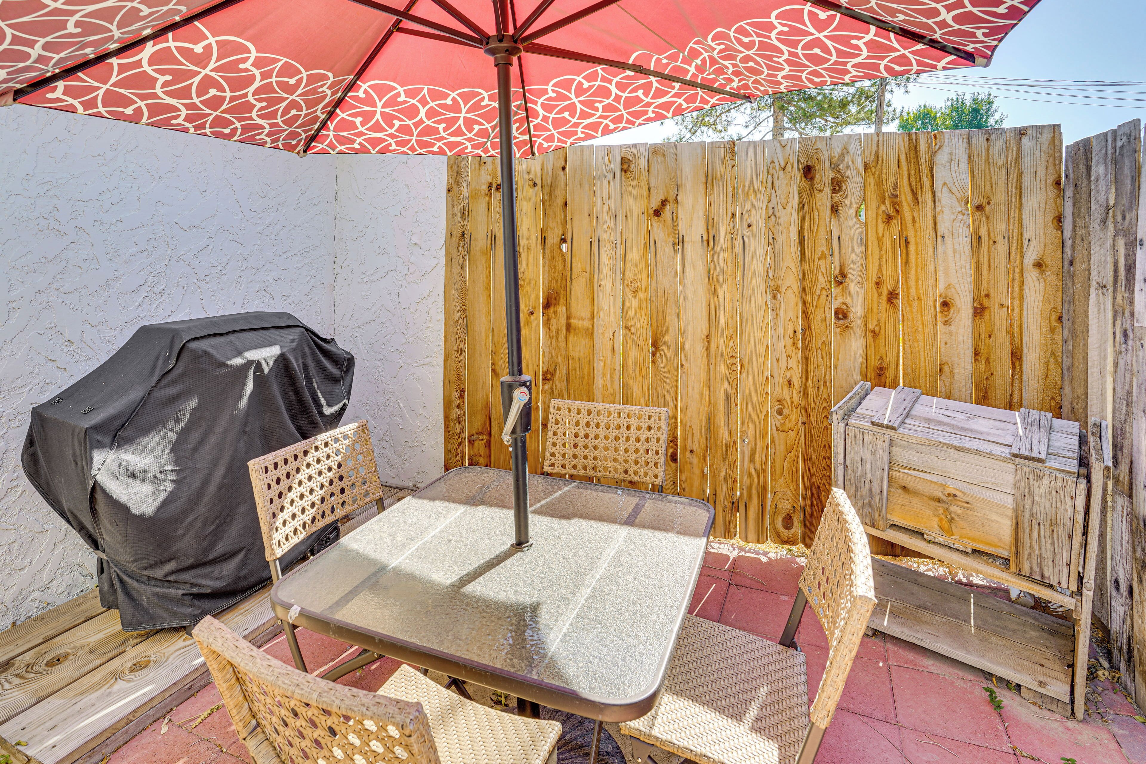 An outdoor patio with a table and chairs, a covered grill, and a wooden fence.