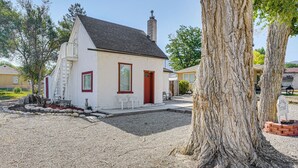 A small white building with a red door and windows, surrounded by gravel and trees.