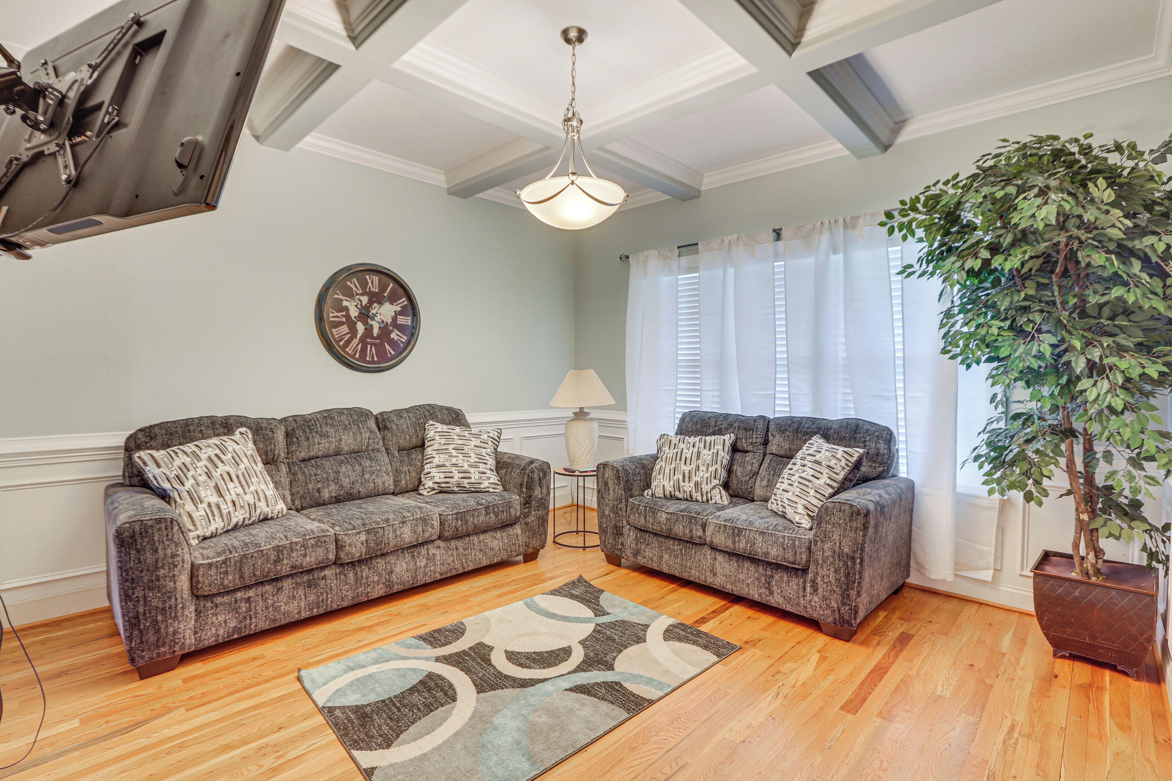 A living room with two grey sofas, a patterned rug, a large plant, a clock, and a ceiling fan.