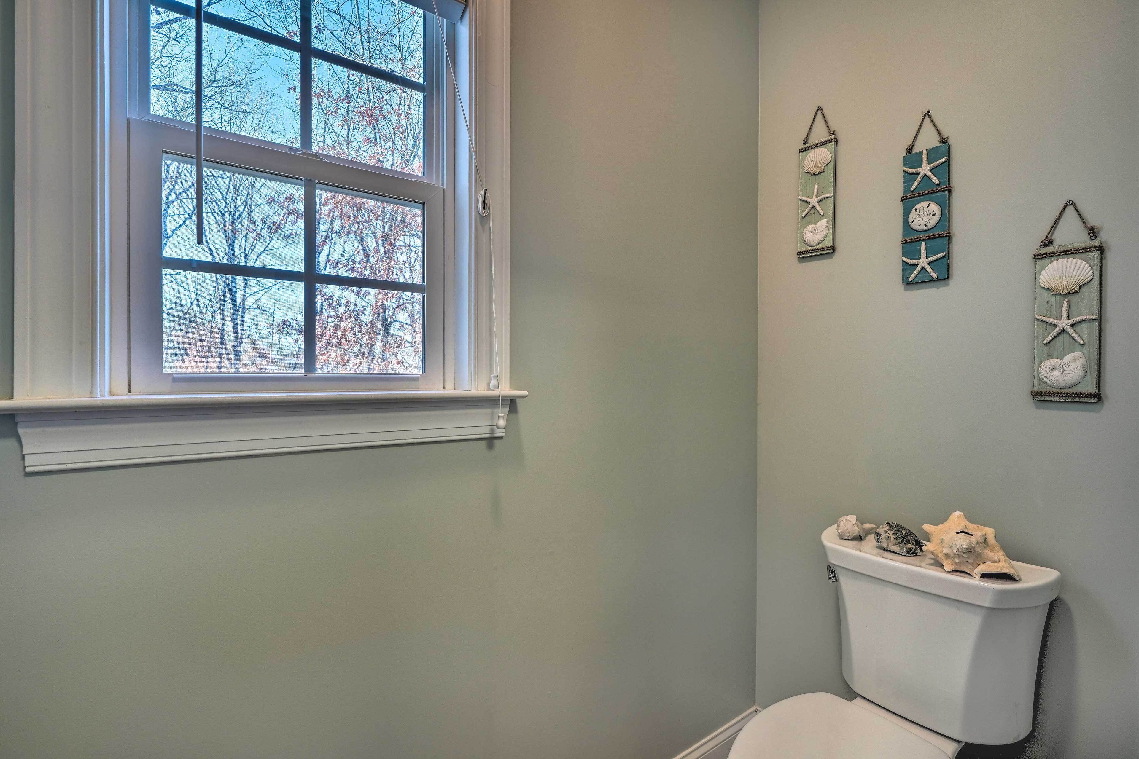 A bathroom with a toilet, a window, and three wall-mounted decorations.