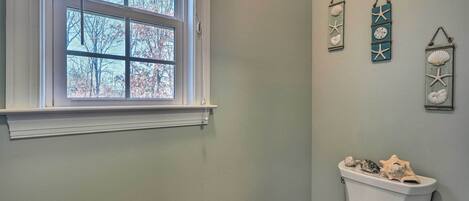 A bathroom with a toilet, a window, and three wall-mounted decorations.