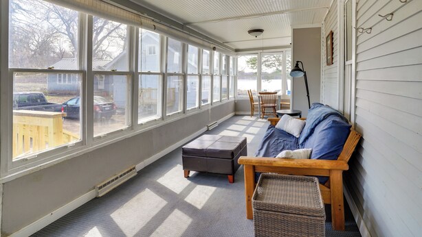 A sunlit room with large windows, a wooden bench, a cushioned bench, and a wicker basket.