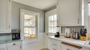 A kitchen with white cabinets, a coffee maker, a toaster, and a window with a view of a wooden deck.