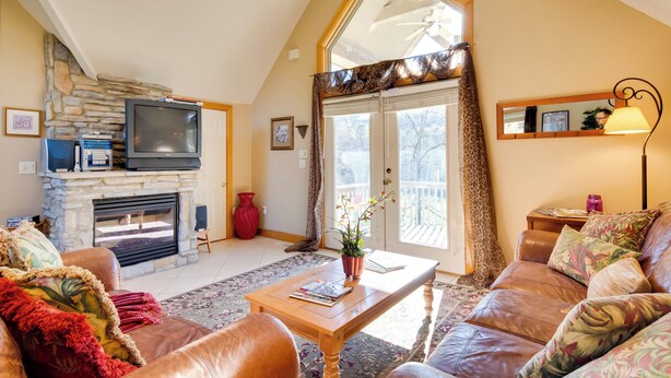 A living room with a stone fireplace, leather sofa, and a television. - Peaceful Lake Lure Cabin w/ Fireplace! (Lake Lure)