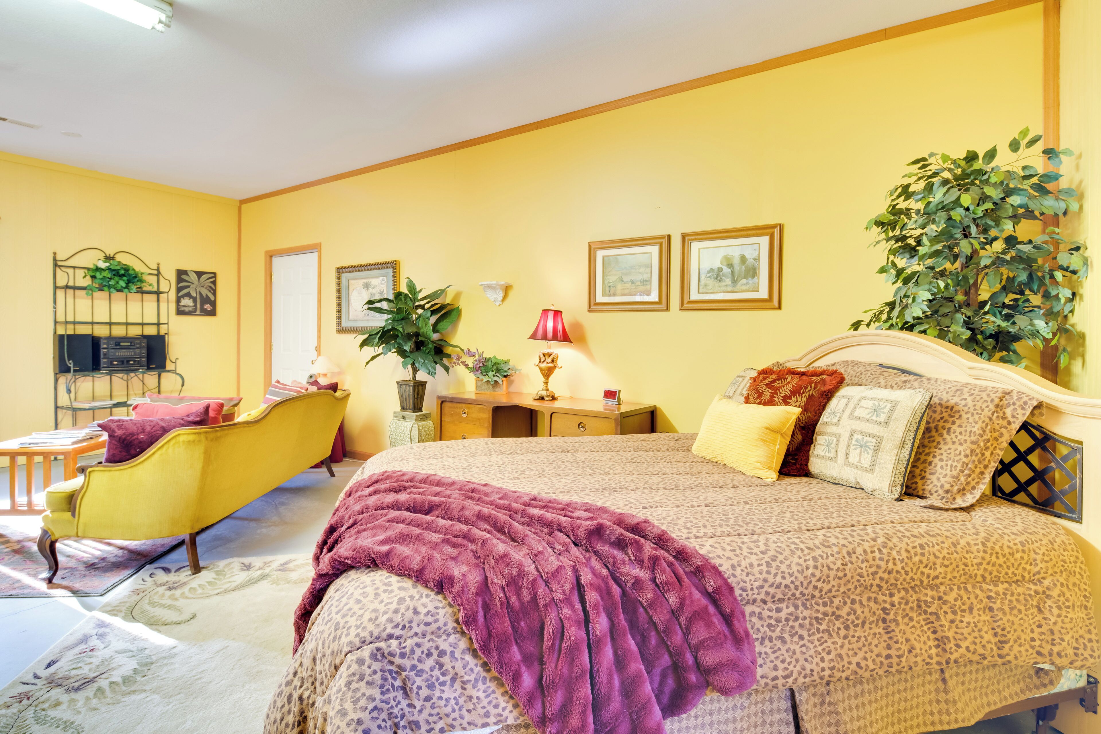 A bedroom with a bed, a nightstand, a lamp, a chair, and a plant.