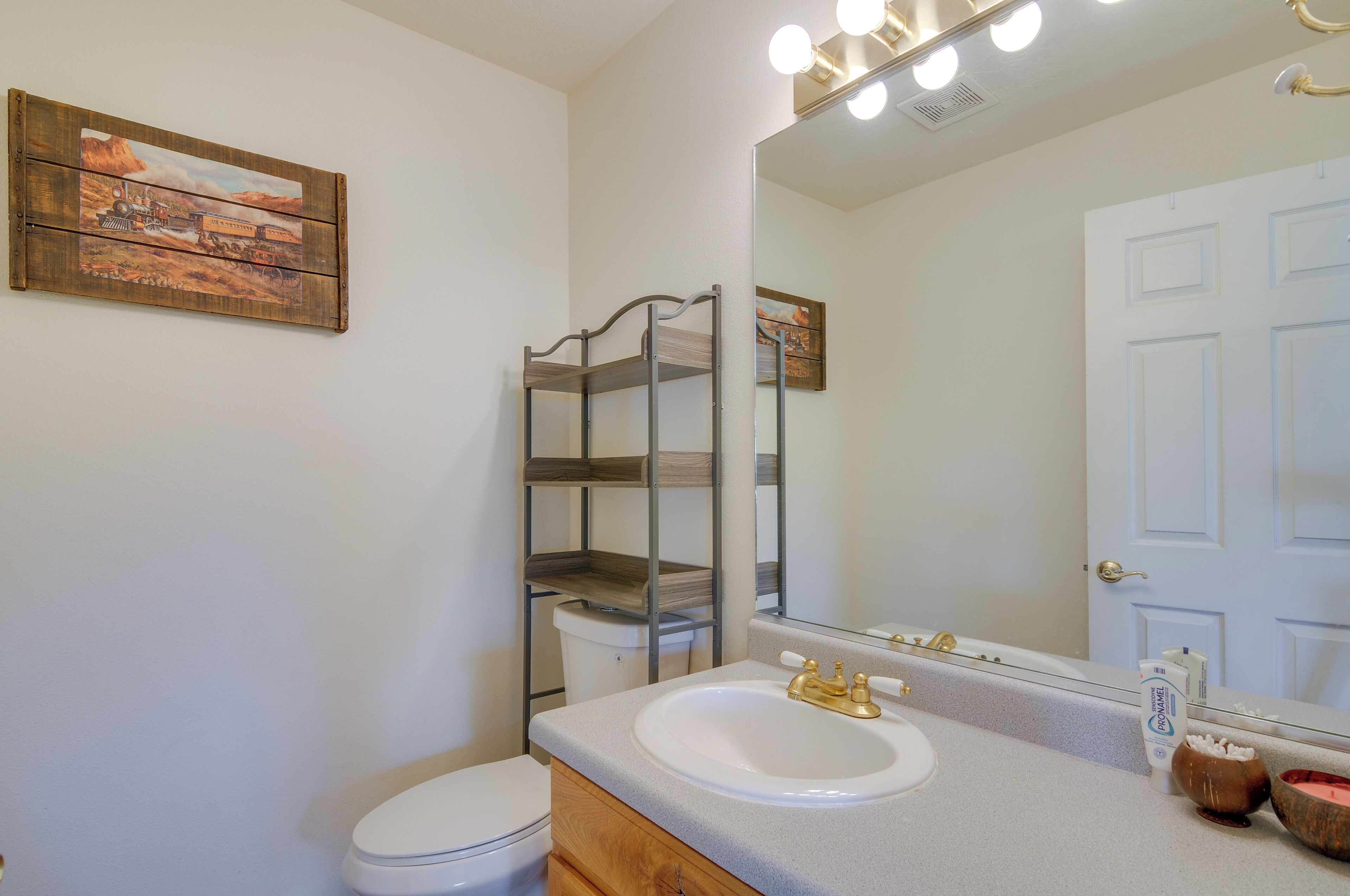 A bathroom with a white sink, a mirror, and a wooden shelf unit.