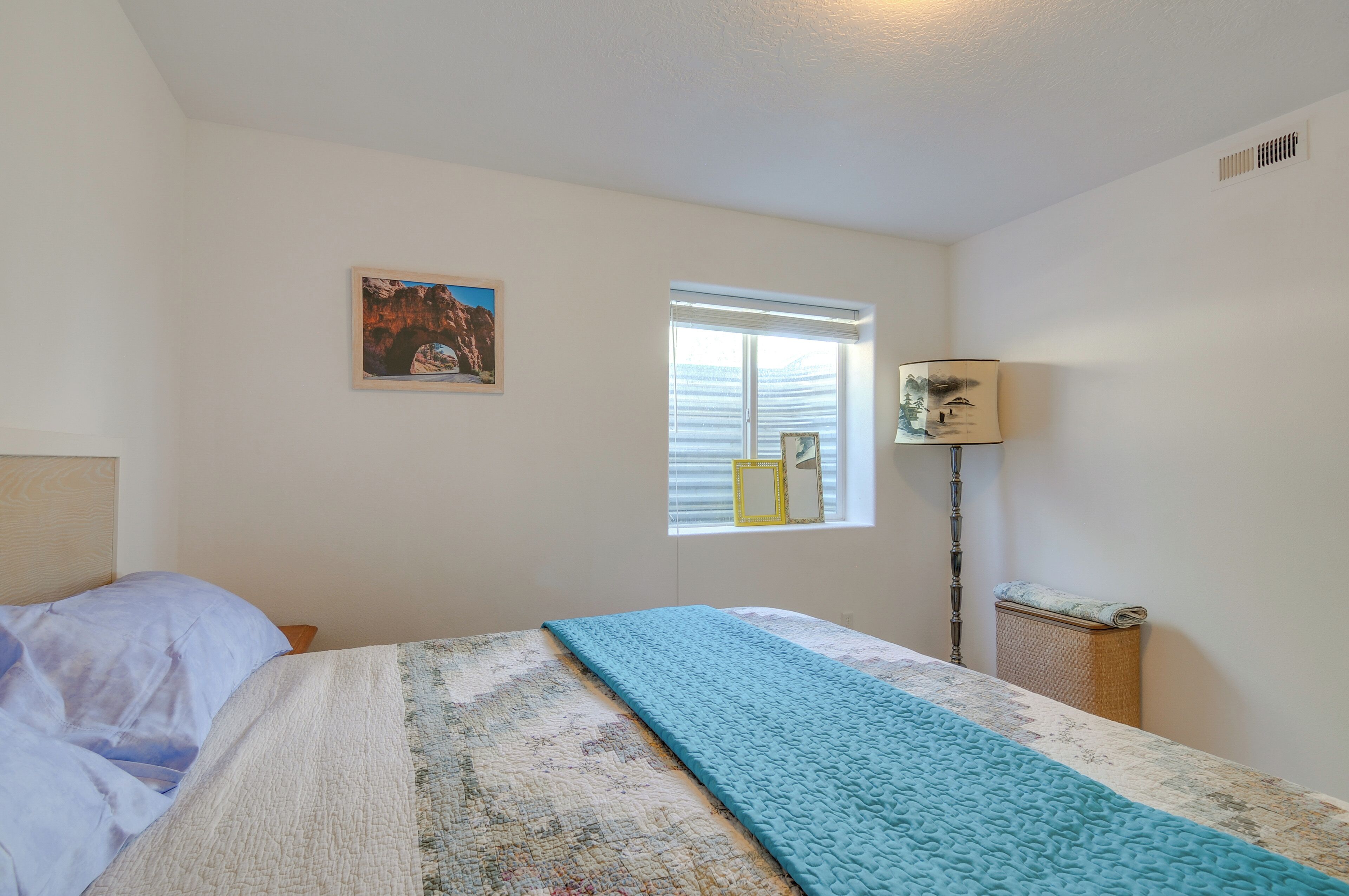 A bedroom with a bed, a window with blinds, a lamp, and a framed picture on the wall.