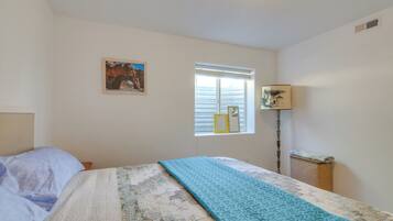 A bedroom with a bed, a window with blinds, a lamp, and a framed picture on the wall.