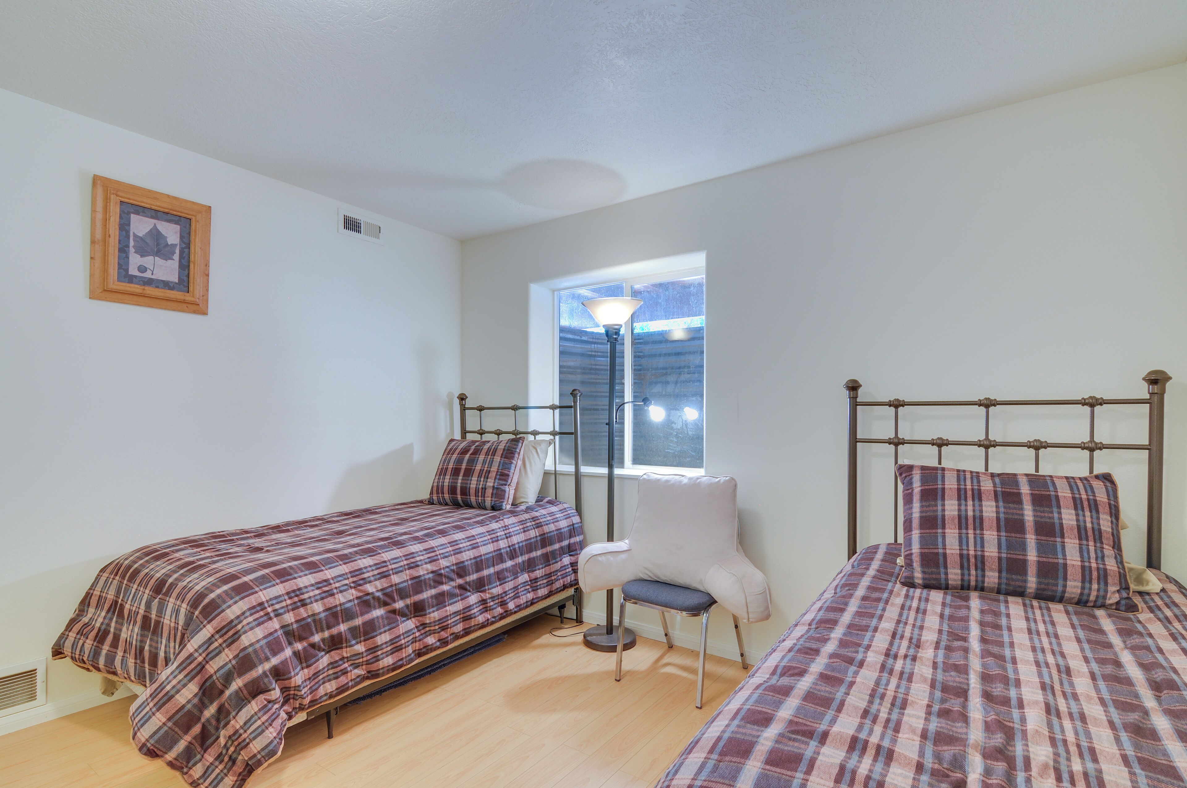 A bedroom with two beds, a chair, a window, and a picture on the wall.