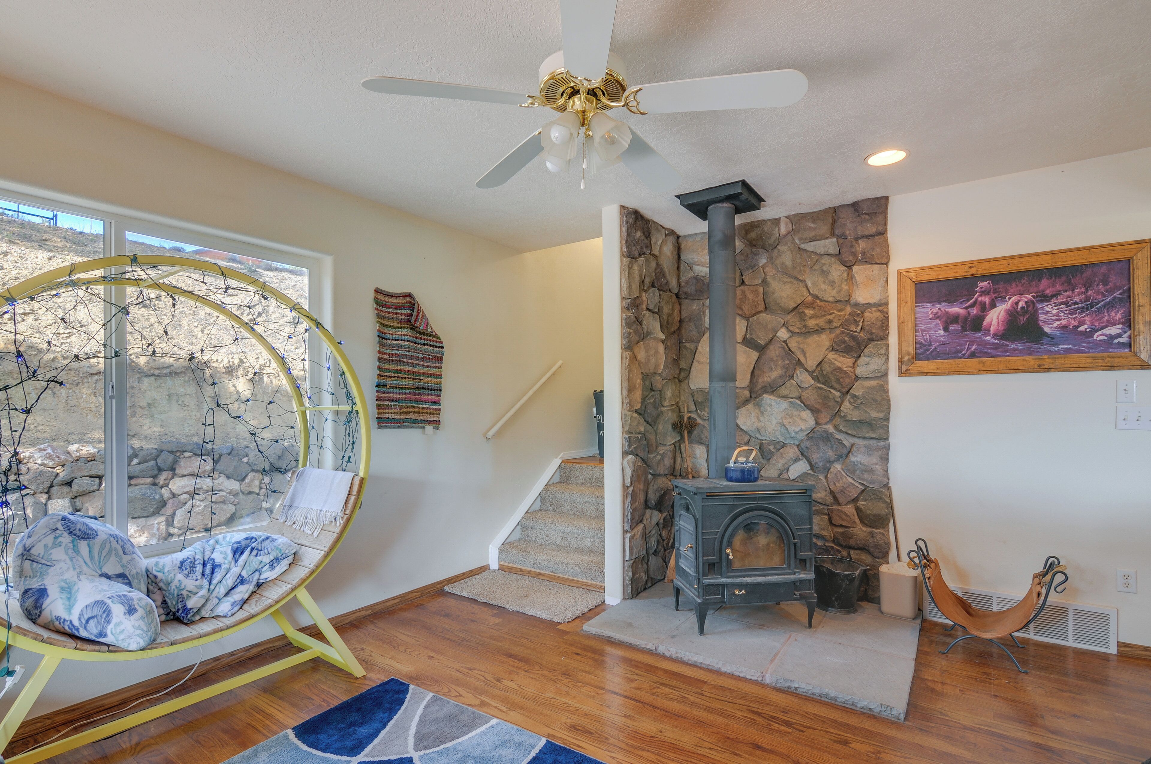 A room with a stone fireplace, a hanging chair, a wooden floor, and a ceiling fan.