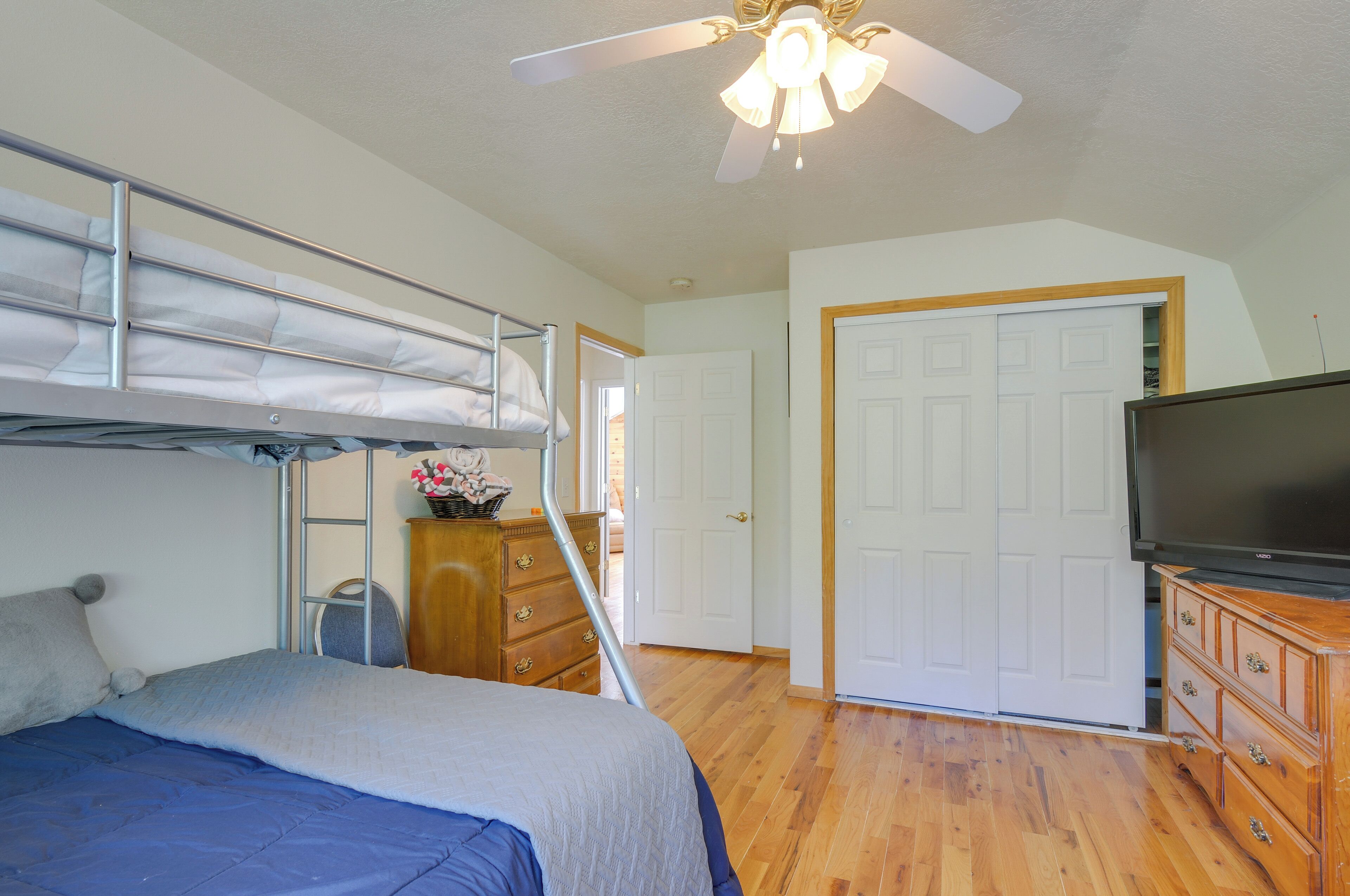 A bedroom with a bunk bed, a dresser, a television, and a ceiling fan.