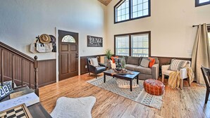 A spacious living room with a high ceiling, wooden floors, and large windows. There are two sofas, a coffee table, and a rug.