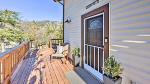 A wooden deck with a rocking chair and potted plants, a door with a window, and a clear view of the surrounding landscape.
