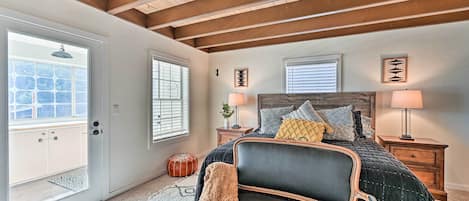 A bedroom with a bed, two bedside tables, a chair, a wooden ceiling, and a door with a window.