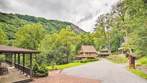 Un chalet doté d’un porche abrité, d’un bâtiment principal et d’une maison d’hôtes, le tout entouré d’une végétation luxuriante et adossé à une chaîne de montagnes.