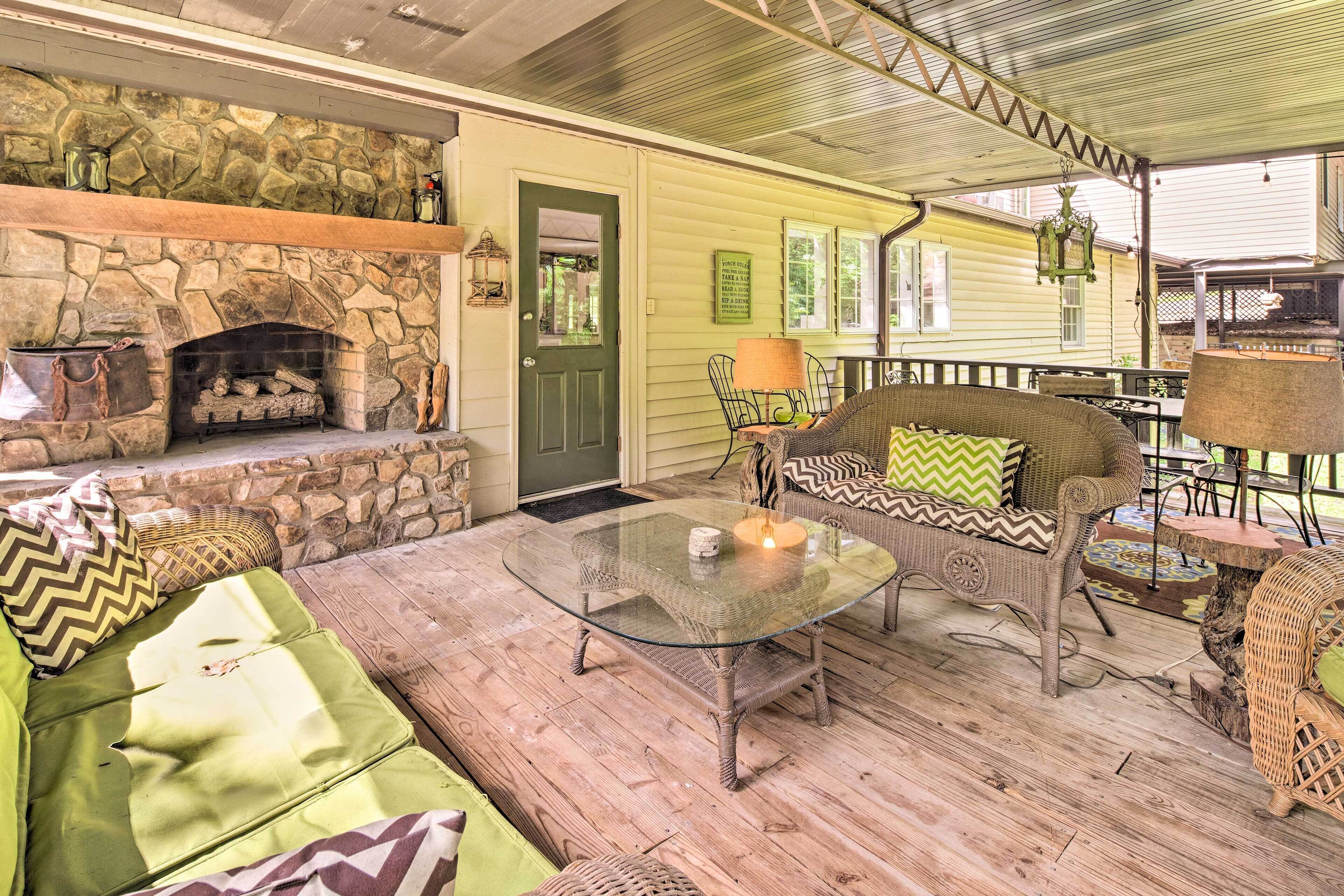 A cozy outdoor seating area with wicker furniture, a glass-top table, and a stone fireplace.