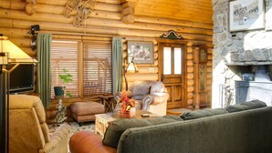A log cabin interior with a fireplace, wooden walls, a sofa, a chair, and a television. - 'lacy's Log Cabin' Alto Home w/ Mountain Views! (Alto)