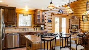 A log cabin kitchen with wooden cabinets, a granite countertop, a stainless steel dishwasher, and a bar area with stools. - 'lacy's Log Cabin' Alto Home w/ Mountain Views! (Alto)