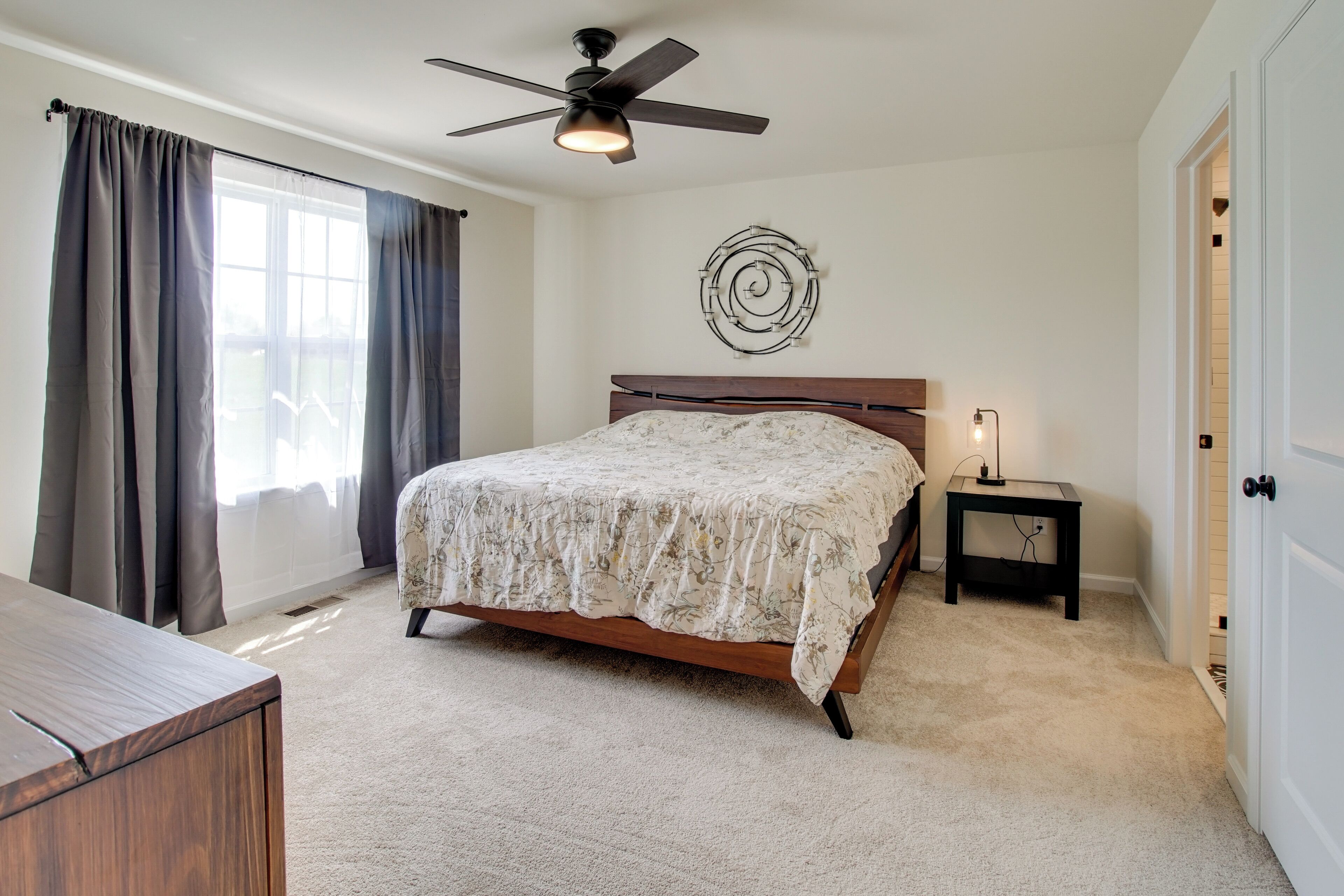 A bedroom with a bed, a ceiling fan, a bedside table with a lamp, and a door.