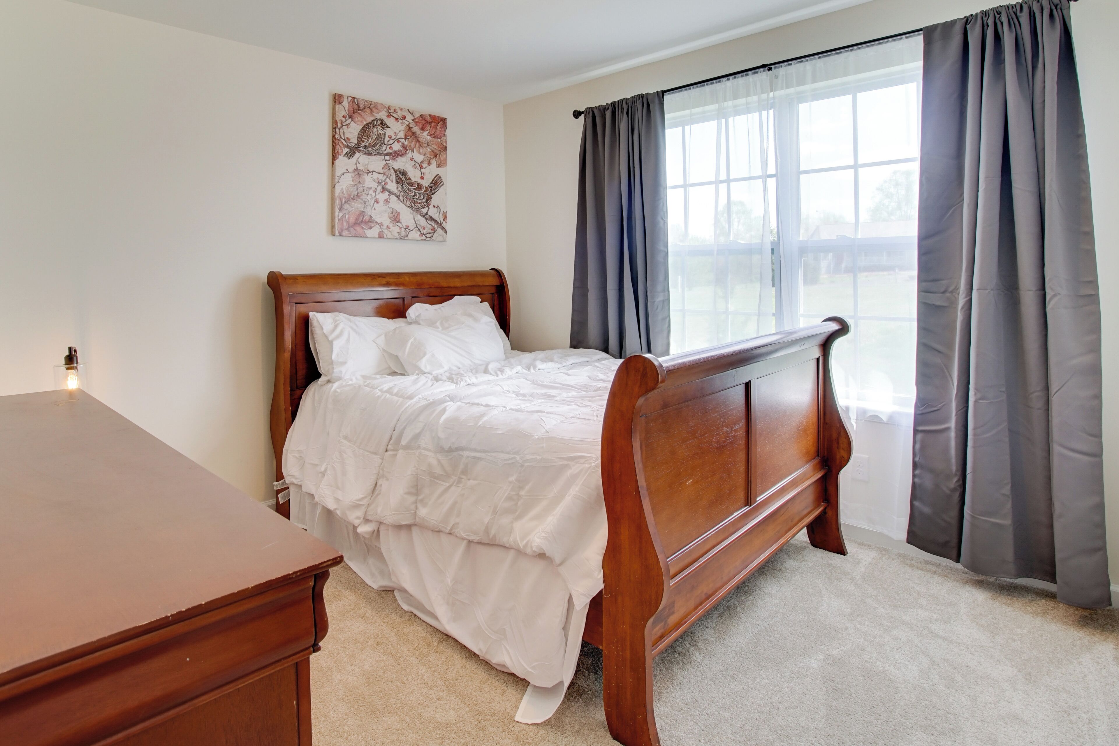 A bedroom with a wooden bed, a nightstand, a wall-mounted lamp, and a window with curtains.