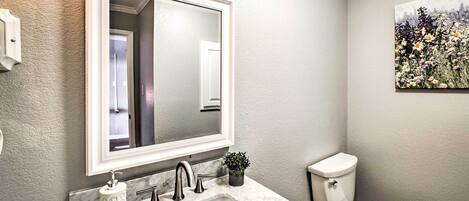 A bathroom with a white sink, a mirror, a toilet, and a small potted plant.