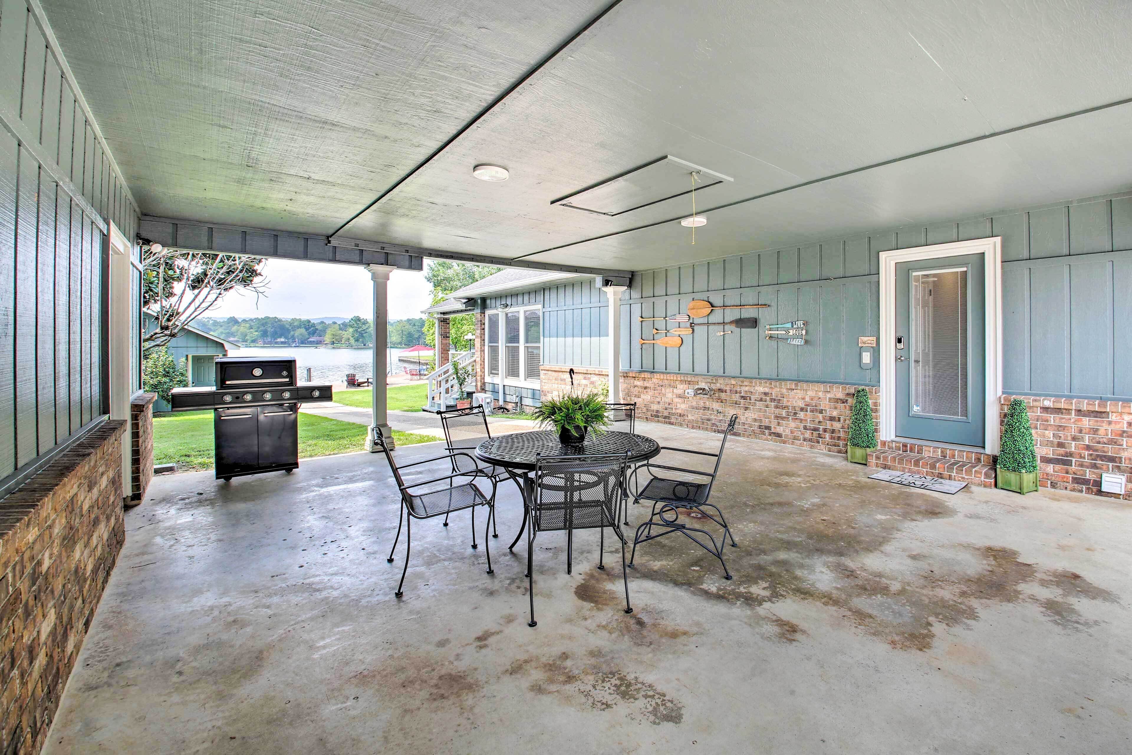A covered patio with a round metal table and chairs, a grill, and a brick wall.
