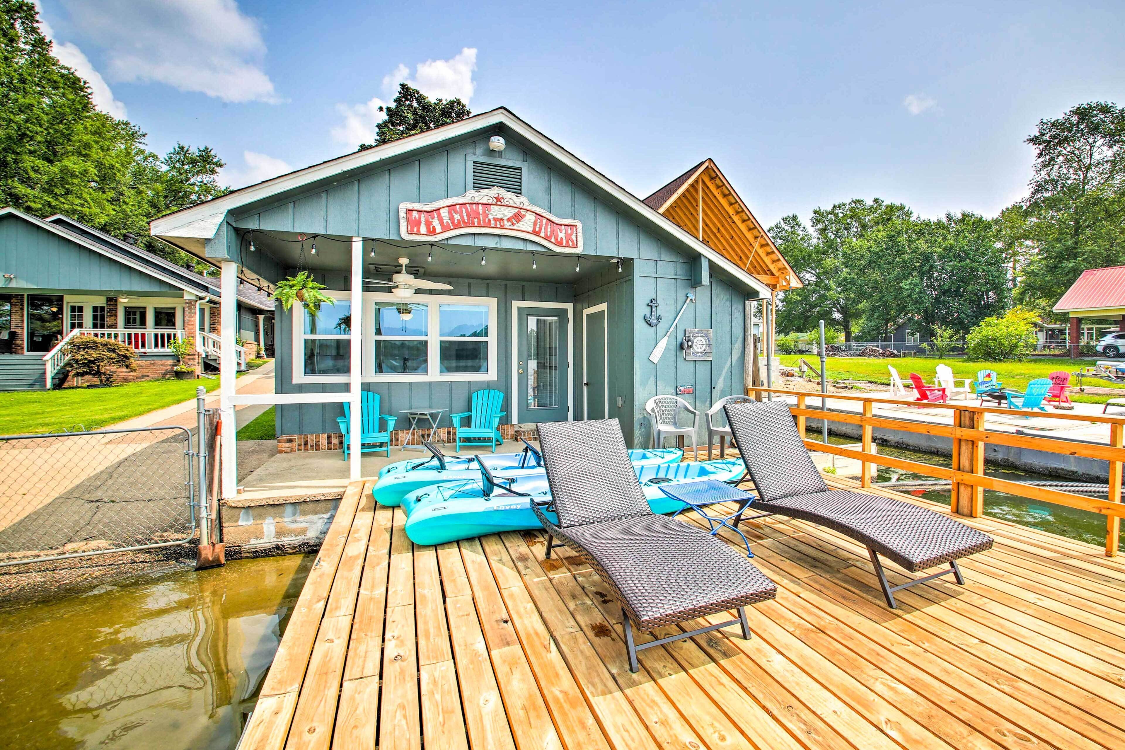 Une terrasse en bois avec des chaises longues et un espace piscine, un bâtiment portant une enseigne indiquant « Whiskey Dock », et une piscine entourée d’une clôture.