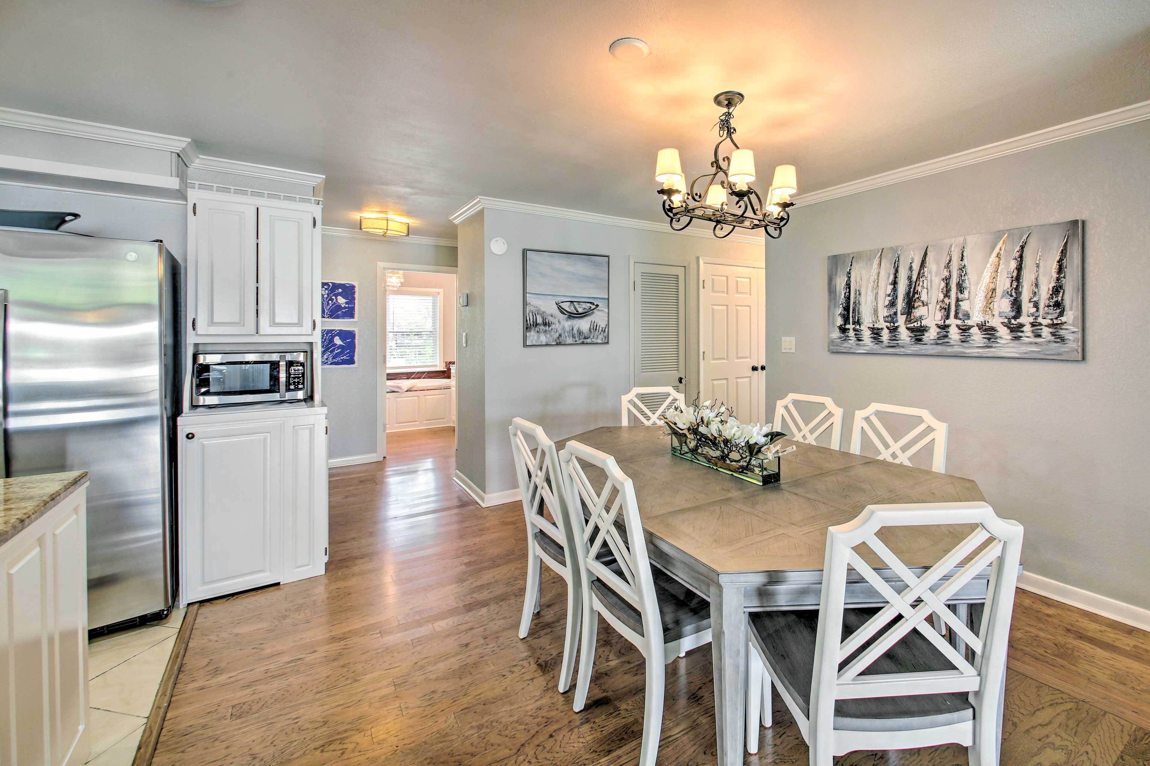 A modern kitchen with white cabinetry, a stainless steel refrigerator, and a wooden dining table with white chairs.