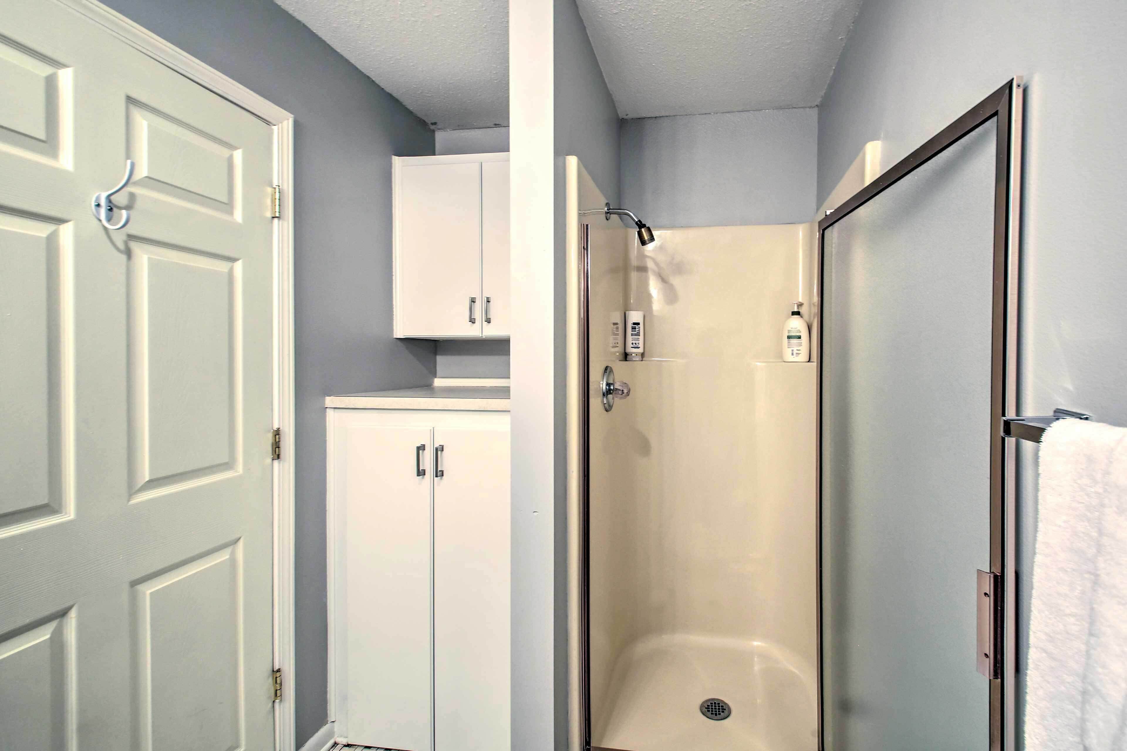 A bathroom with a shower, a toilet, and a sink. There is a cabinet above the toilet.