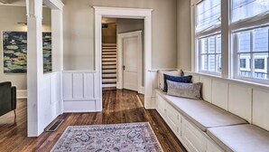 A hallway with a wooden floor, a white bench with cushions, and a large window. - Immaculate Birmingham House w/ Covered Porch! (Birmingham)