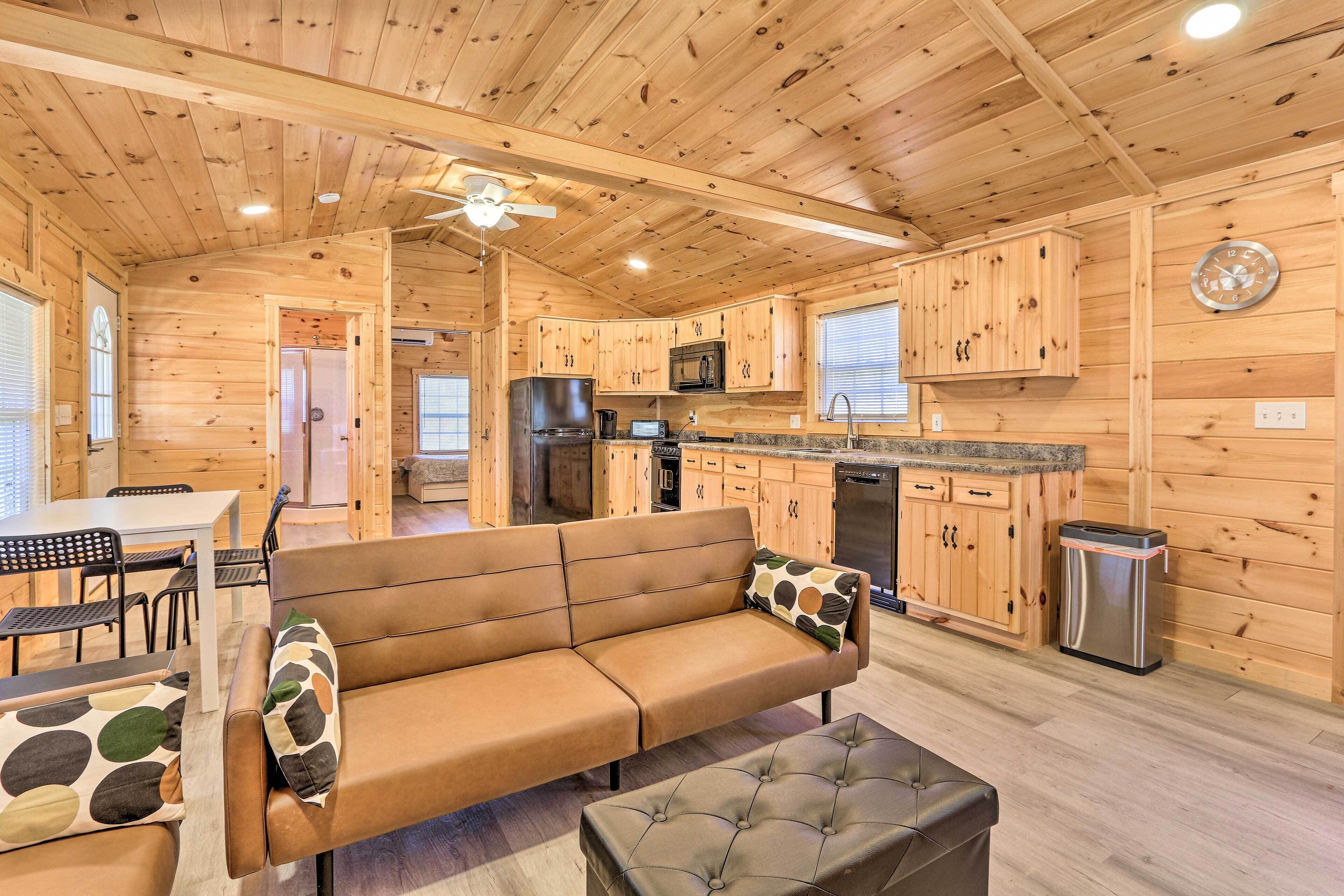 A cozy cabin-style room with a wooden interior, a sofa, a dining table, and a kitchenette.