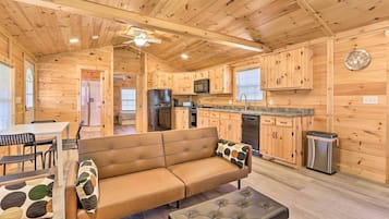 A cozy cabin-style room with a wooden interior, a sofa, a dining table, and a kitchenette.