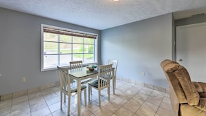 A dining area with a table and chairs, a window with blinds, and a ceiling light fixture. - 'loretta' Sun-kissed Apt on Country Music Hwy (Hagerhill)