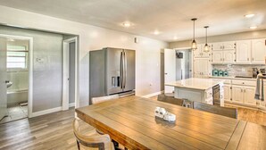 Een moderne keuken met een houten eettafel, witte kasten en roestvrijstalen apparatuur.