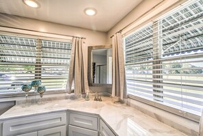 Une salle de bain dotée d’un grand meuble-lavabo, d’un miroir et d’une fenêtre avec des stores.