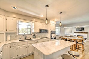 Une cuisine moderne avec des meubles blancs, un grand îlot central et des luminaires suspendus.