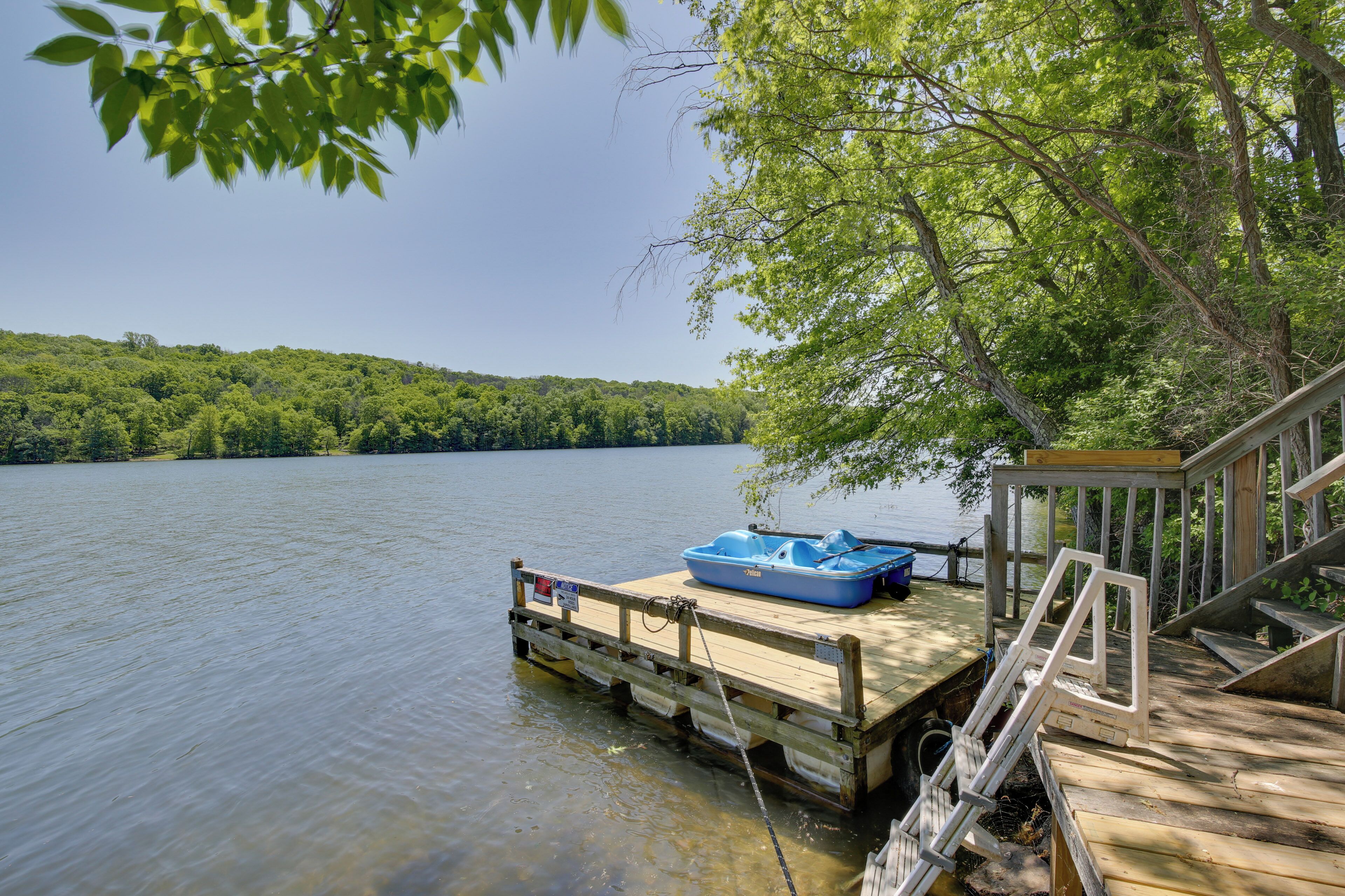 A wooden dock extending into a calm lake with a blue boat docked on it.