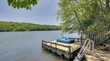 A wooden dock extending into a calm lake with a blue boat docked on it.