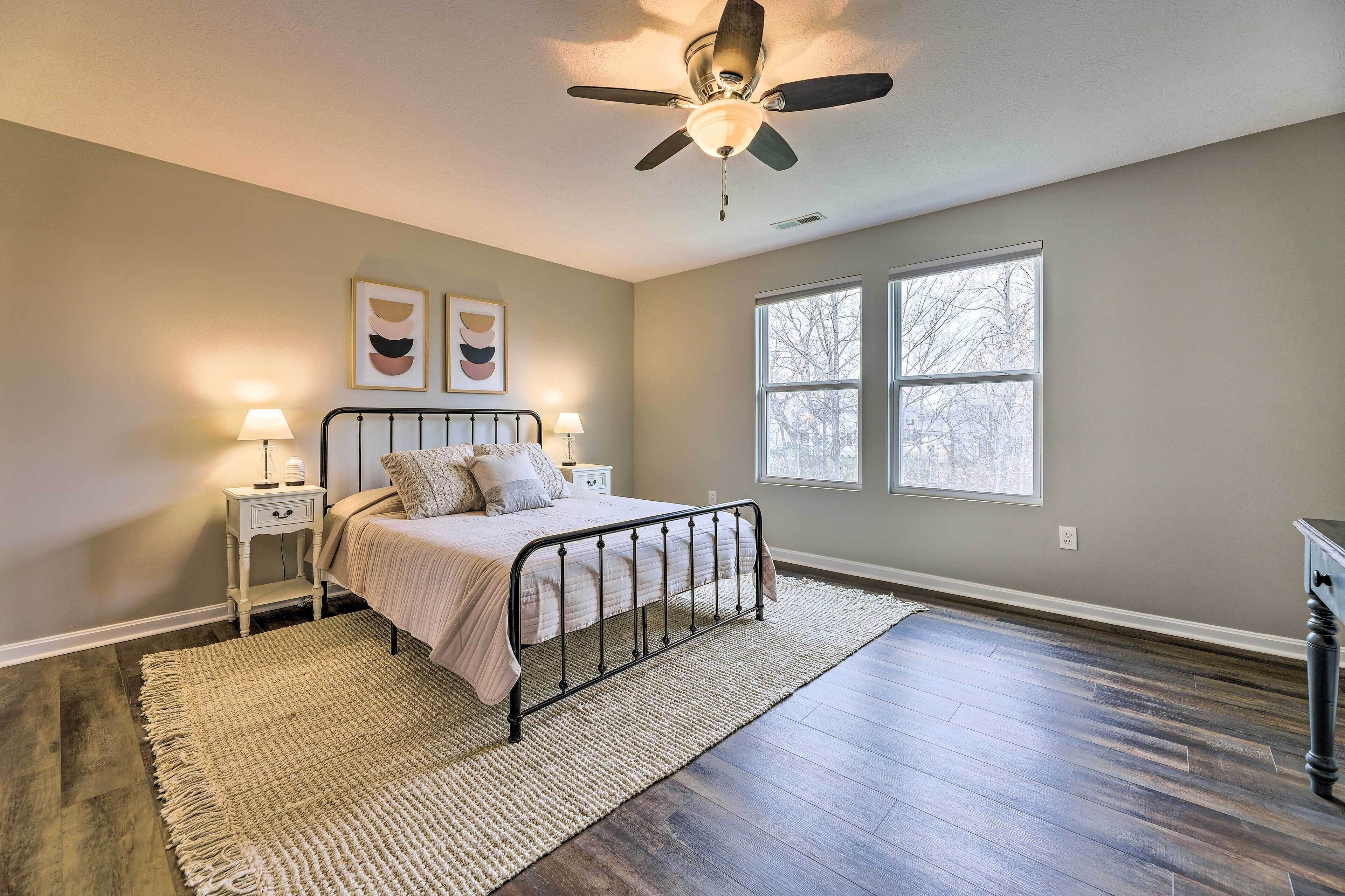 A bedroom with a bed, nightstands, a ceiling fan, and two windows.