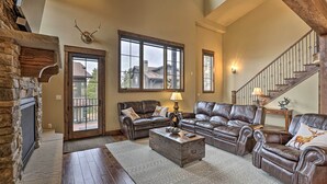 Un salón amplio con sofás de cuero, chimenea, ventanas grandes y una escalera.
